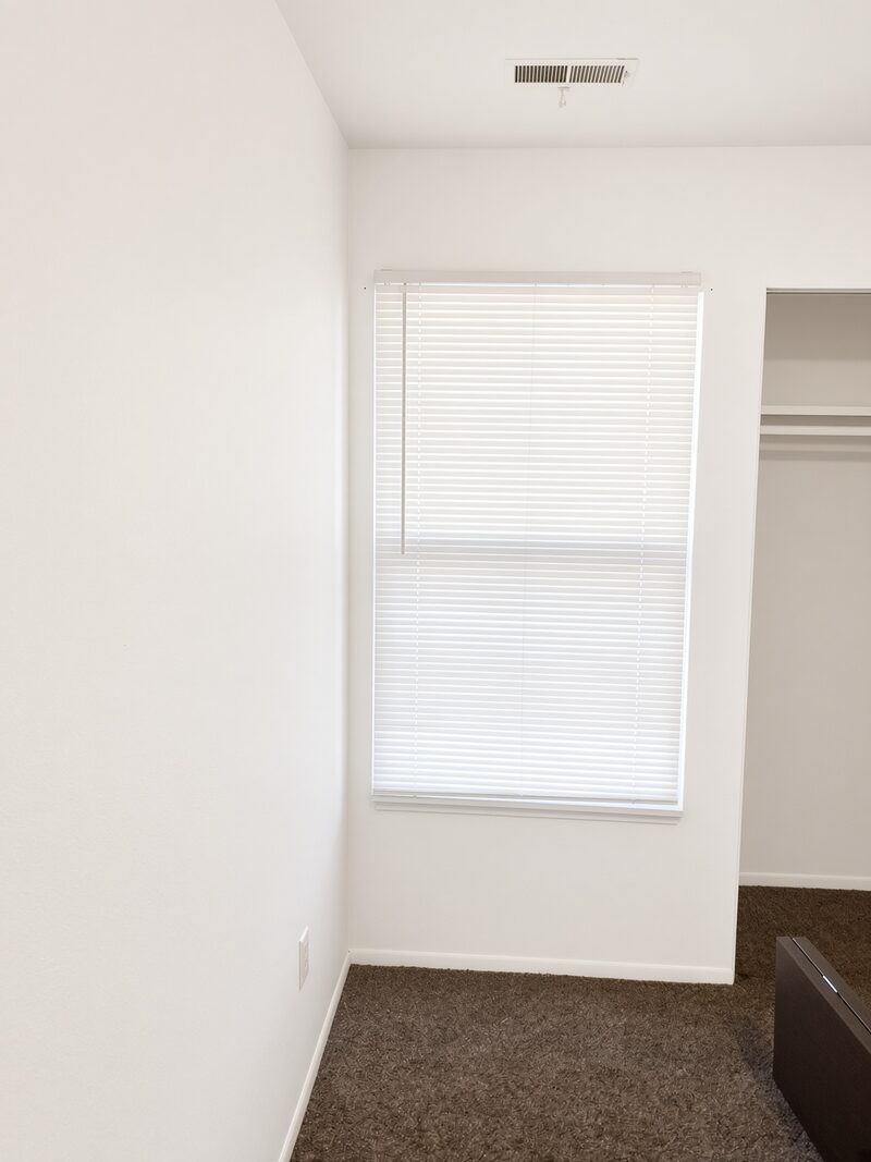 Bedroom corner with a window and a closet opening, walls rolled flat.