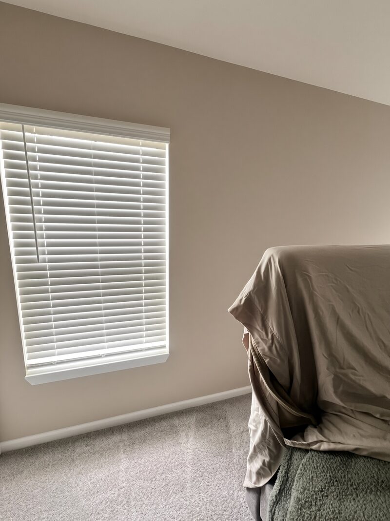 Window and blinds on a greige wall with the furniture covered.