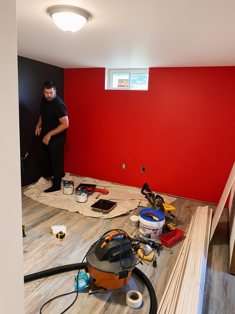 Red accent wall beside a dark wall, drop cloth still down.