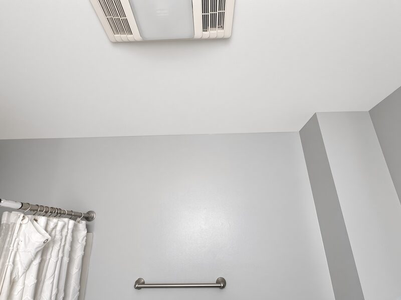 Grey bathroom wall under a white ceiling, cut in clean around the fan and down the corner.